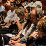 Dans la salle, le public prend des notes, un casque sur les oreilles.