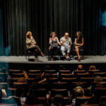 Devant le rideau bleu sombre d’une salle de cinéma, Marie Gaumy, Liliana Tavares (directrice de COM Acessibilidade Comunicacional, Recife), Livia Motta (directrice de Ver com Palavras, Sao Paulo) animent un débat traduit par Emerson Silva.