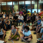 Debouts, assis sur des chaises, des canapés ou par terre, une trentaine de personnes valides et handicapées visuelles écoutent attentivement.