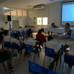 Dans la pénombre d’une salle de conférence, des lycéens sont assis devant un écran de cinéma allumé. Marie Gaumy est assise sous l’écran et anime l’atelier.